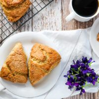 Two Earl Grey Scones on a plate sitting by a wire cooling rack full of fresh baked scones.