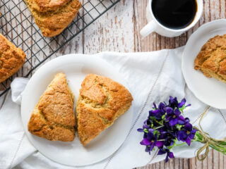 Two Earl Grey Scones on a plate sitting by a wire cooling rack full of fresh baked scones.