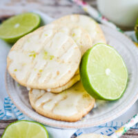 Key Lime Pie Shortbread Cookies stacked on a white plate with slices of lime.