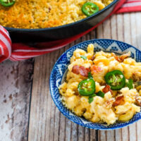 A blue and white bowl full of jalapeno bacon mac and cheese next to a skillet.
