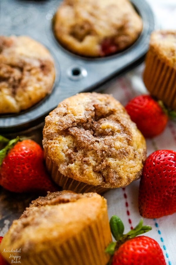 A close up shot of a strawberry rhubarb muffin next to a muffin tin and some fresh strawberries. 