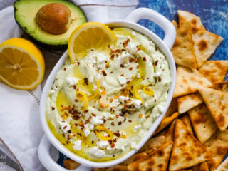 A white serving bowl of lemon feta dip surrounded by pita chips.