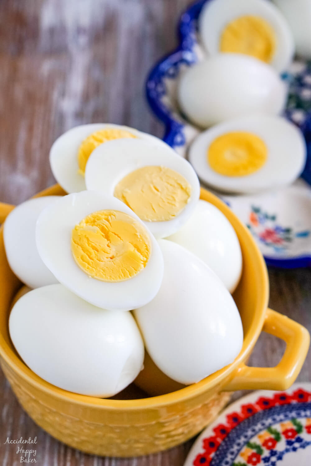 A yellow bowl full of hard boiled eggs, with a few sliced hard boiled eggs laying on top. 