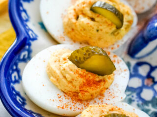 Deviled eggs with a sprinkle of cayenne pepper and a slice of pickle on each egg.